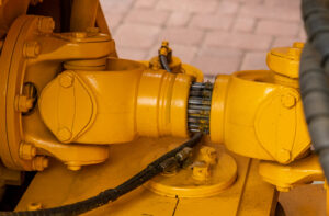 A yellow industrial drivetrain with a paved surface in the background. Hydraulic lines are connected to the component.