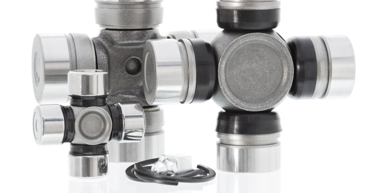 Three universal joints of varying sizes are positioned upright against a white background. A wire is lying on the surface.