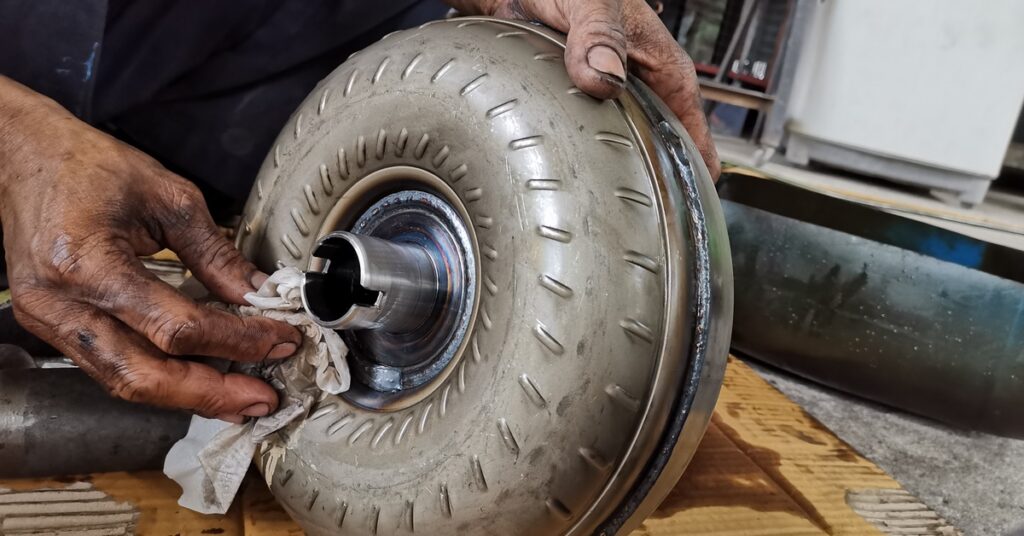 A close-up of a person cleaning a torque converter with a cloth. The person's hands are covered in oil.