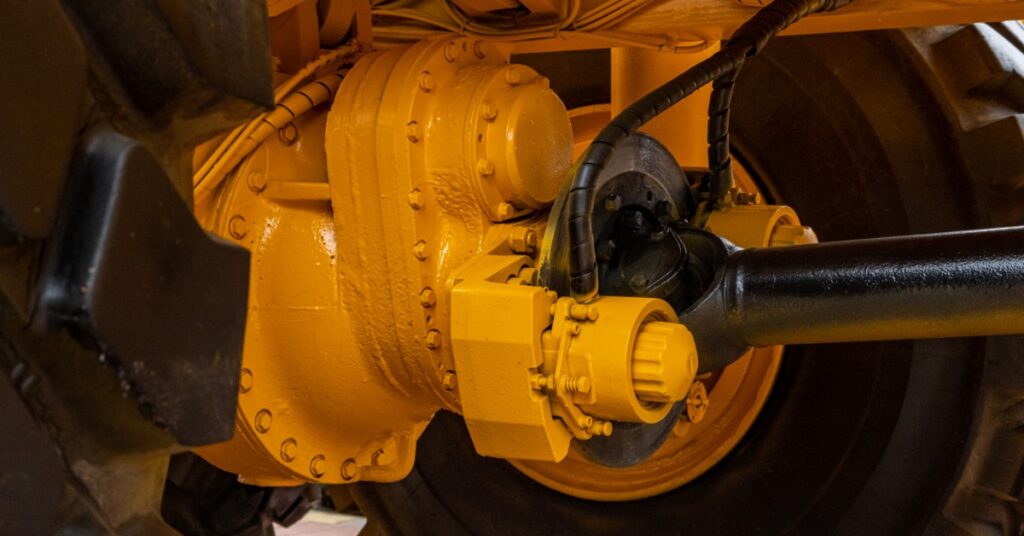 A close-up of a yellow, heavy-duty drivetrain on a mining vehicle. A large tire is in the background.