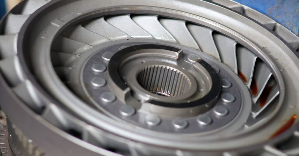 A metallic torque converter component with central splines, radial blades, and an outer ring on a work surface.
