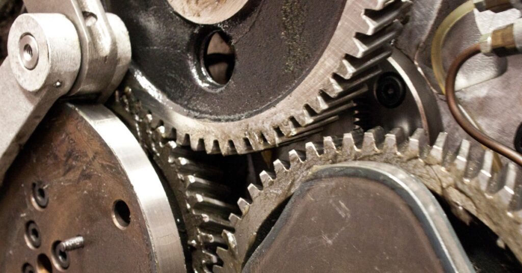 An extreme close-up of a group of metallic gears, shafts, and toothed wheels overlapping on a dark machine.
