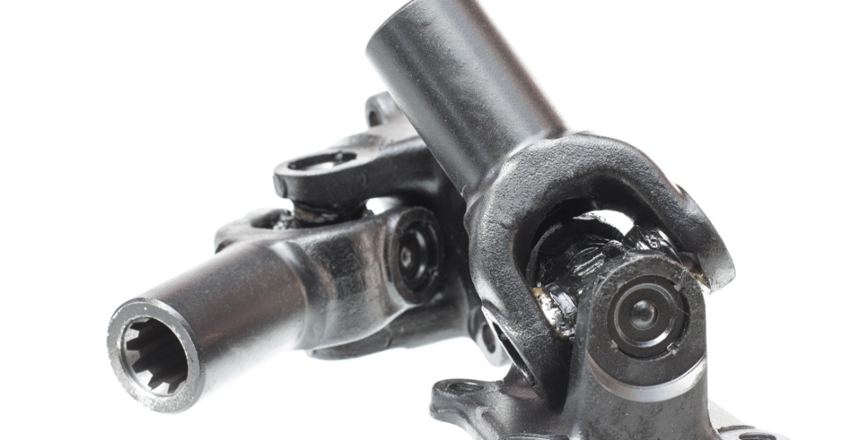 A black metal universal joint assembly with round shafts, bolt holes, and greased hinge parts on a white background.