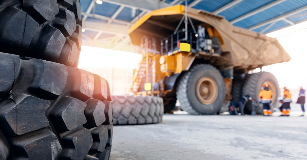 Large mining truck tires standing on a concrete floor with workers nearby inside a bright industrial garage.