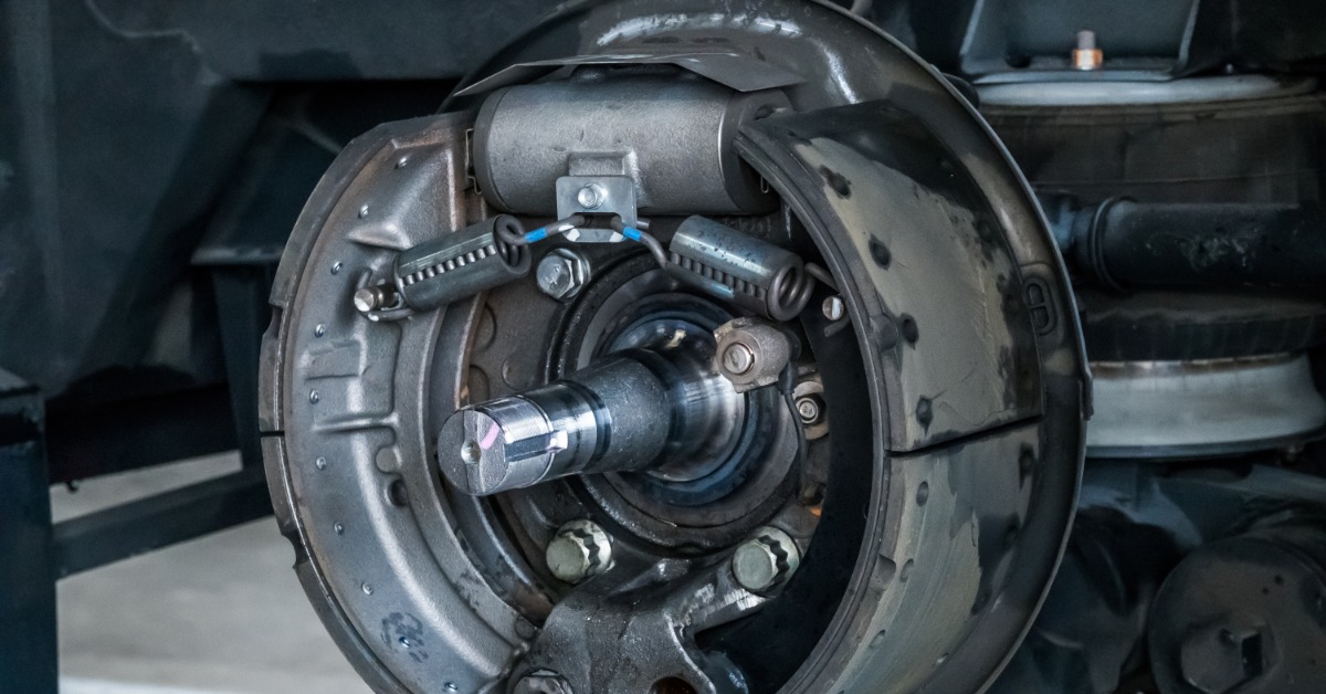 A gray drum brake assembly with springs, bolts, curved shoes, and a central black axle sits under a vehicle.