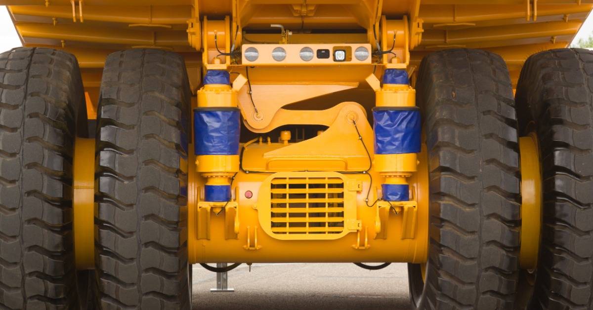 A yellow dump truck underside shows several large black tires, blue cylindrical covers, and a gridded rear panel.